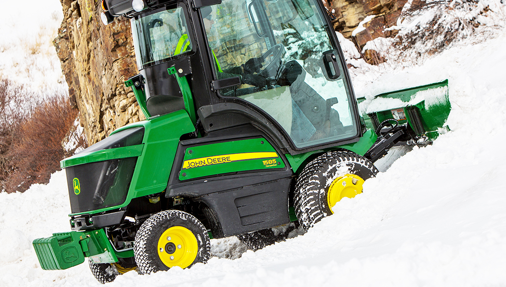 John Deere tractor with a plow being operated by a man in a high visibility vest to remove snow